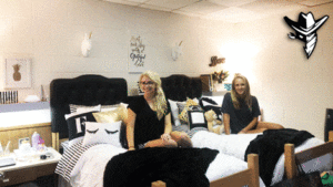 Two women sitting on a bed in a room.