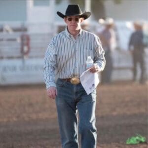 A man in cowboy hat and jeans walking across the dirt.