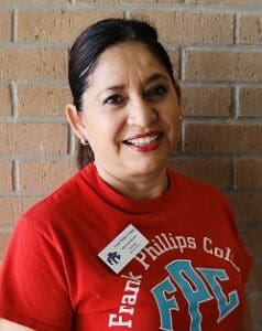 A woman in red shirt standing next to brick wall.