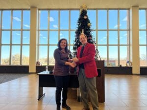 A man and woman are shaking hands in front of a christmas tree.