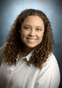 A woman with curly hair and white shirt smiling.